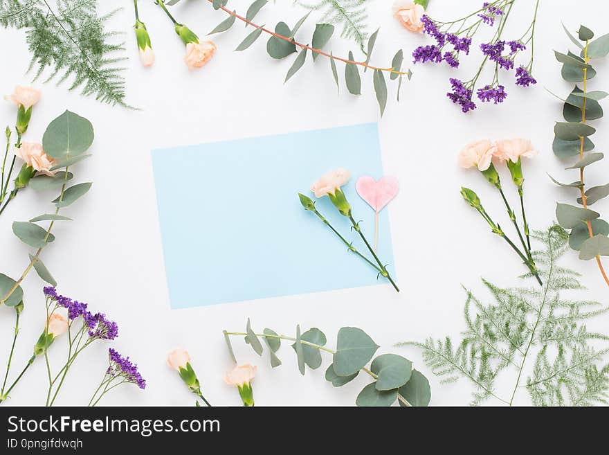 Flowers composition. Paper blank, carnation flowers, eucalyptus branches on pastel  background. Flat lay, top view, copy spaceFlat