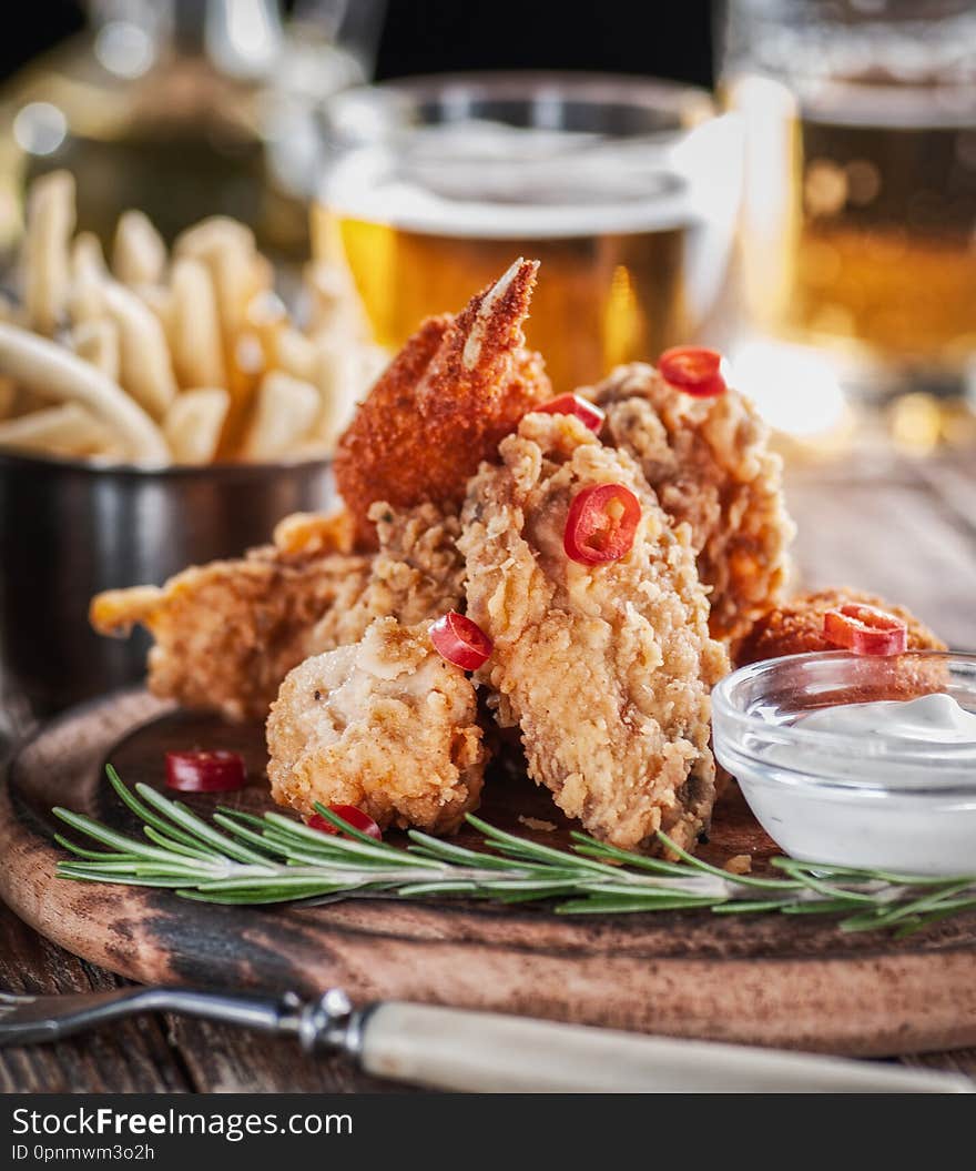 Chicken wings in a batter with beer and fries on a wooden plate with sauce