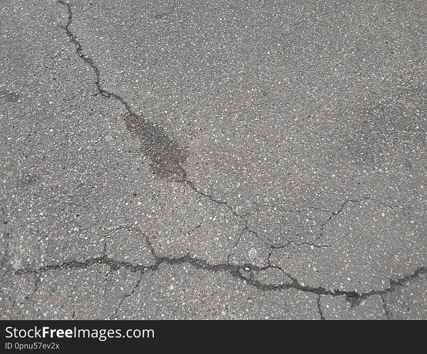 An old, worn asphalt pathway with multiple fractures on the surface. An old, worn asphalt pathway with multiple fractures on the surface.