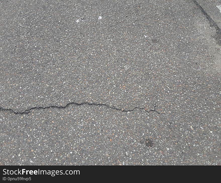 An old, worn asphalt pathway with multiple fractures on the surface. An old, worn asphalt pathway with multiple fractures on the surface.