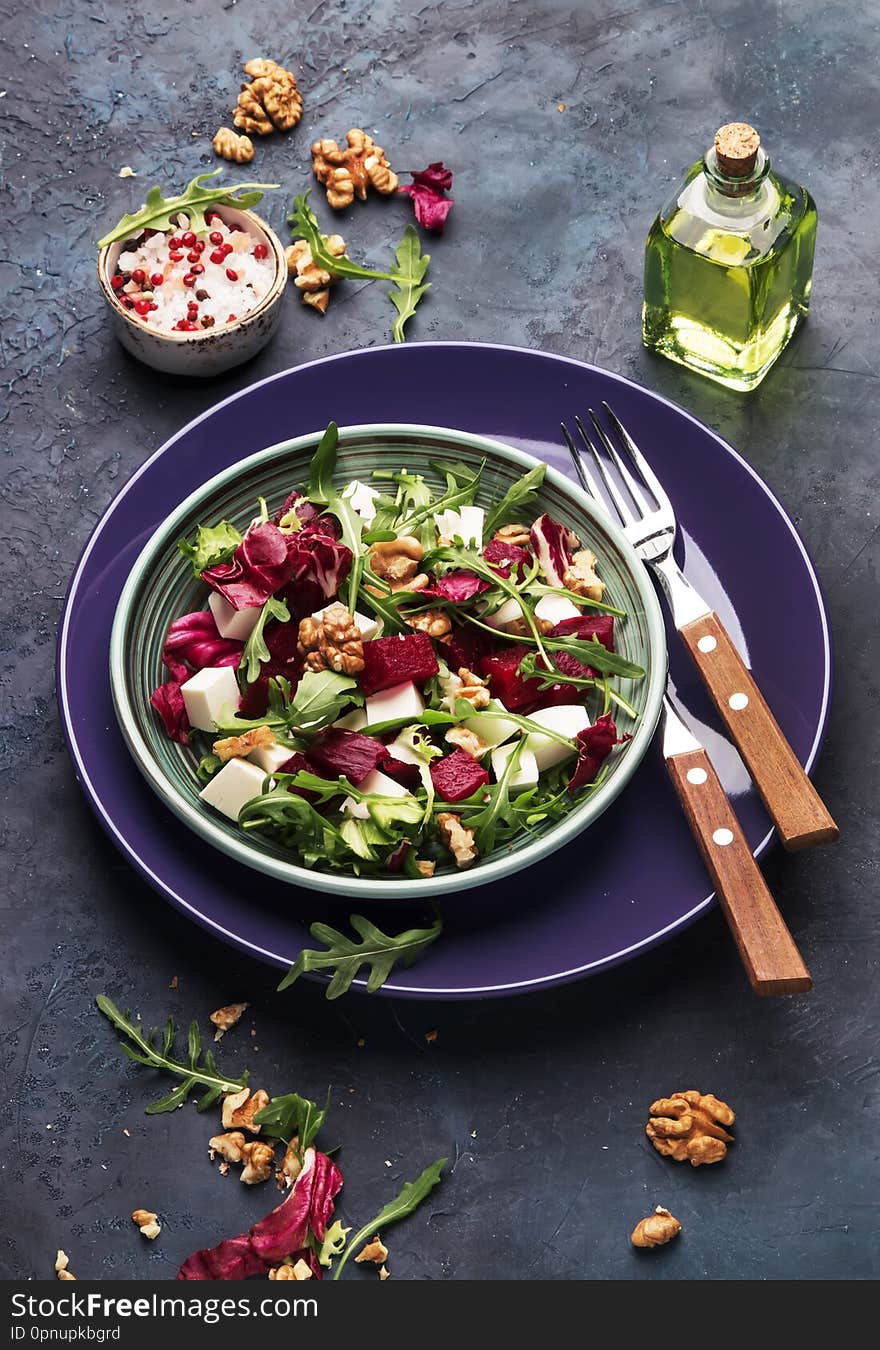 Beet Or Beetroot Salad With Fresh Arugula, Radicchio, Soft Cheese And Walnuts On Plate With Fork, Dressing And Spices On Blue