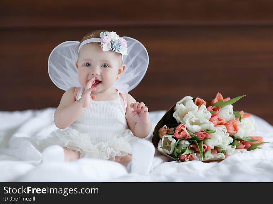 Blue-eyed baby with angel wings behind him.Baby Newborn with Angel Wings. Child Sitting at Blue Sky Cloud. Girl 5-7 months sitting on a white bed in the bedroom.Cute newborn angel. Blue-eyed baby with angel wings behind him.Baby Newborn with Angel Wings. Child Sitting at Blue Sky Cloud. Girl 5-7 months sitting on a white bed in the bedroom.Cute newborn angel