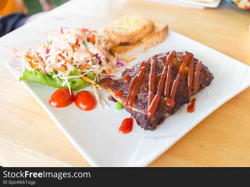 Close up view of pork barbecue ribs with barbecue sauce that served with garlic bread and vegetable salad