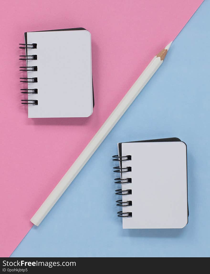 Two open spiral notebooks and a white pencil pencil on a pink and blue diagonal background. Flat lay with copy space. Two open spiral notebooks and a white pencil pencil on a pink and blue diagonal background. Flat lay with copy space