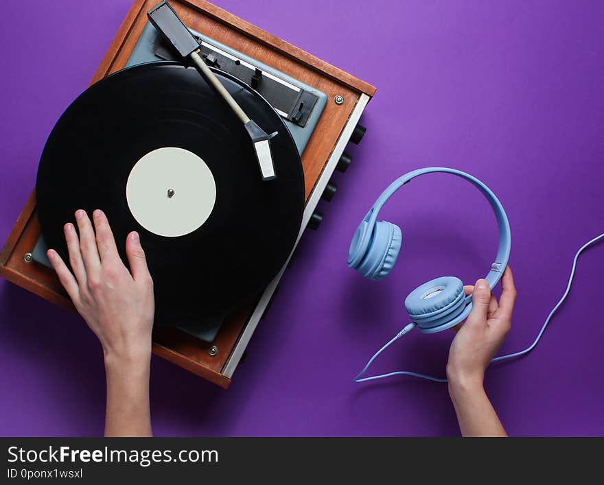 DJ concept. Female hands uses vinyl player and holds the headphones in her hand against purple background. Retro style. Pop culture. Top view