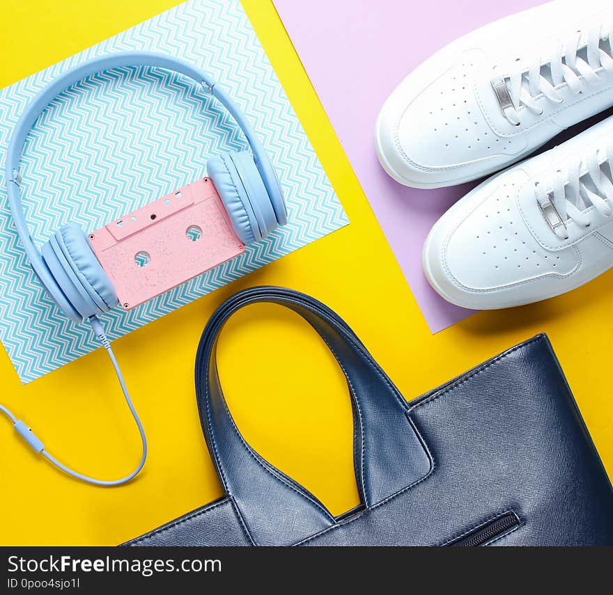 Retro 80s old fashioned objects on a creative background. White sneakers, headphones with audio cassette, women&#x27;s leather bag. Top view. Flat lay