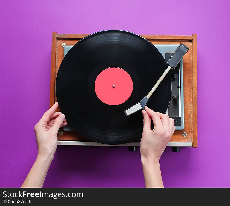 Female hands set up retro vinyl record player with plate on purple background. Top view