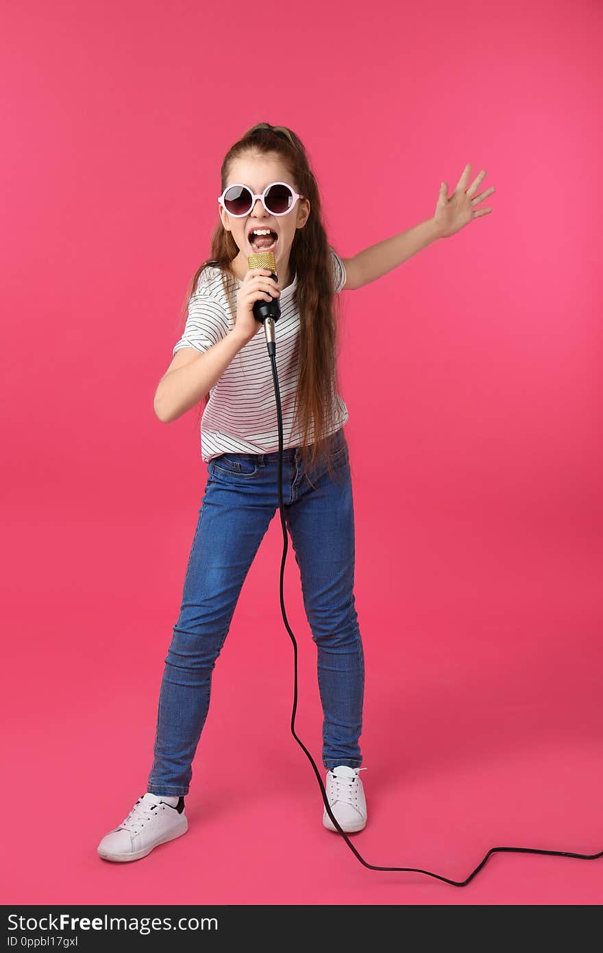 Cute girl singing in microphone on color background