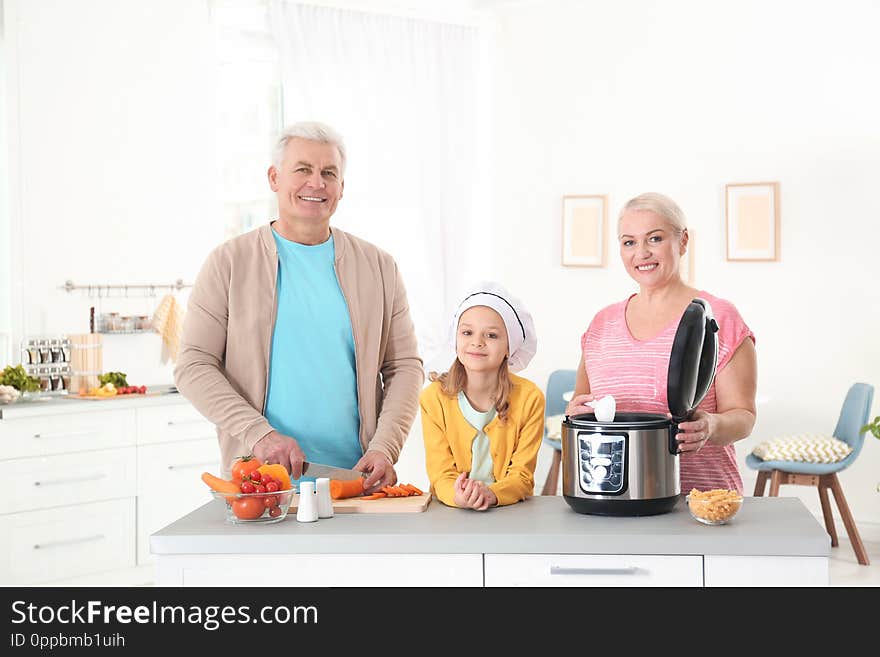 Mature couple and their granddaughter preparing food with modern multi cooker in kitchen