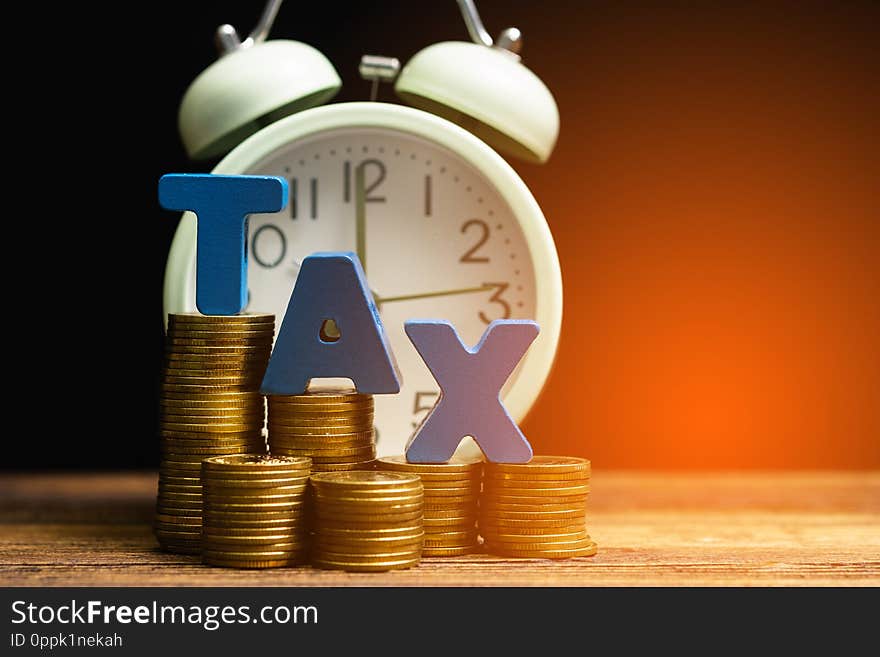 Time to pay TAX concept. TAX alphabet with stack of coin and vintage alarm clock on wooden working table in dark background