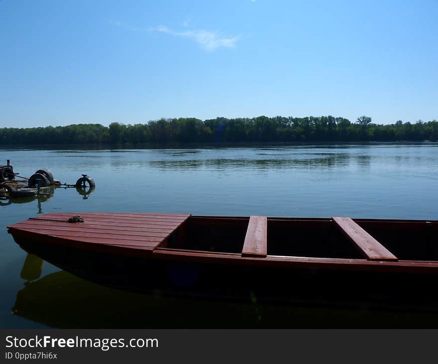 Small red fishing boat detail on quiet river in spring time with tree line on the far side of the river and blue sky above. tranquil scene. outdoors and fresh air concept. boat on the Danube with reflections. Small red fishing boat detail on quiet river in spring time with tree line on the far side of the river and blue sky above. tranquil scene. outdoors and fresh air concept. boat on the Danube with reflections.