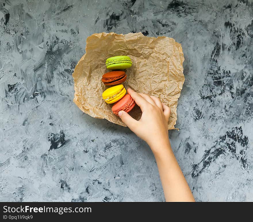 Tasty colorful fresh macaroons and hand child on gray table. Tasty colorful fresh macaroons and hand child on gray table