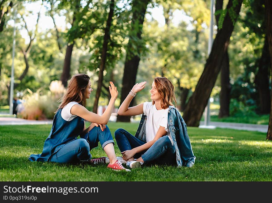 Happy female friends raising hands up giving high five sitting on green grass lawn on sunny day, outdoors in city park. Happy female friends raising hands up giving high five sitting on green grass lawn on sunny day, outdoors in city park