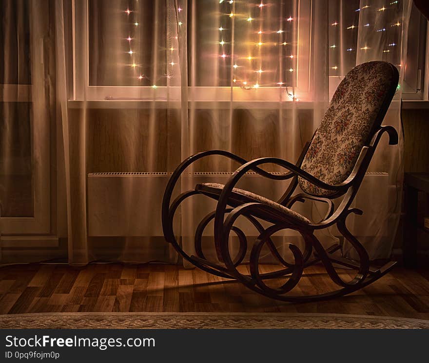 A rocking chair stands by the window in the evening light. A rocking chair stands by the window in the evening light