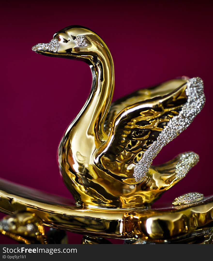 Golden figurine of a single swan close-up on a red background. Golden figurine of a single swan close-up on a red background