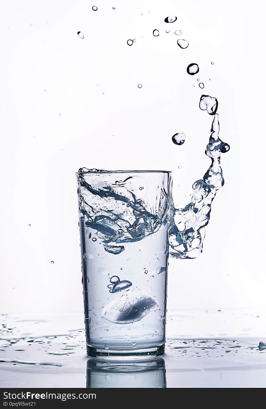 Piece of ice fell into a glass beaker with water. Splashes, white background. Piece of ice fell into a glass beaker with water. Splashes, white background