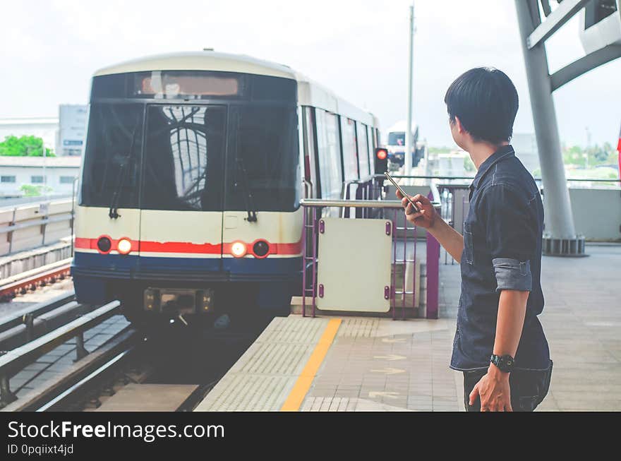 A Asian man passenger using smartphone and looking BTS in train station ,skytrain wait on BTS Skytrain station