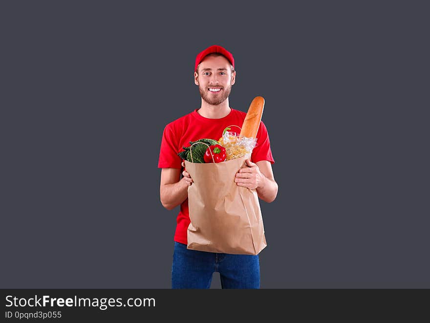 Delivery man holding paper bag with food products on dark background