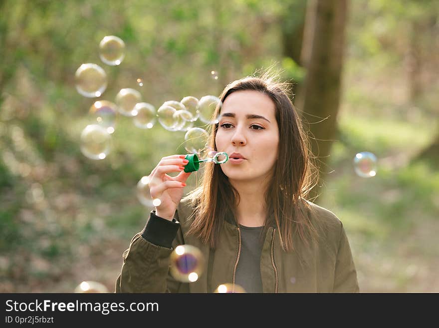 Young woman blowing soap bubbles in the woods. Freedom, lifestyle and networking concept. Colorful vintage analog film look.