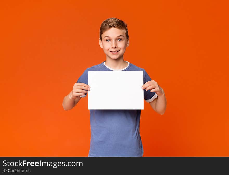 Friendly teen boy holding white blank placard with empty space for your text or product, orange background. Friendly teen boy holding white blank placard with empty space for your text or product, orange background