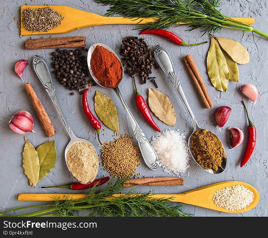 Different spices in wooden and metall spoons on grey background. Bay leaf. Garlic. Fennel. Mustard seeds. Zira. Red pepper. Ginger root. Black pepper. Carnation. Pepper pods. Cinnamon. Salt. Sesame seed. Different spices in wooden and metall spoons on grey background. Bay leaf. Garlic. Fennel. Mustard seeds. Zira. Red pepper. Ginger root. Black pepper. Carnation. Pepper pods. Cinnamon. Salt. Sesame seed.