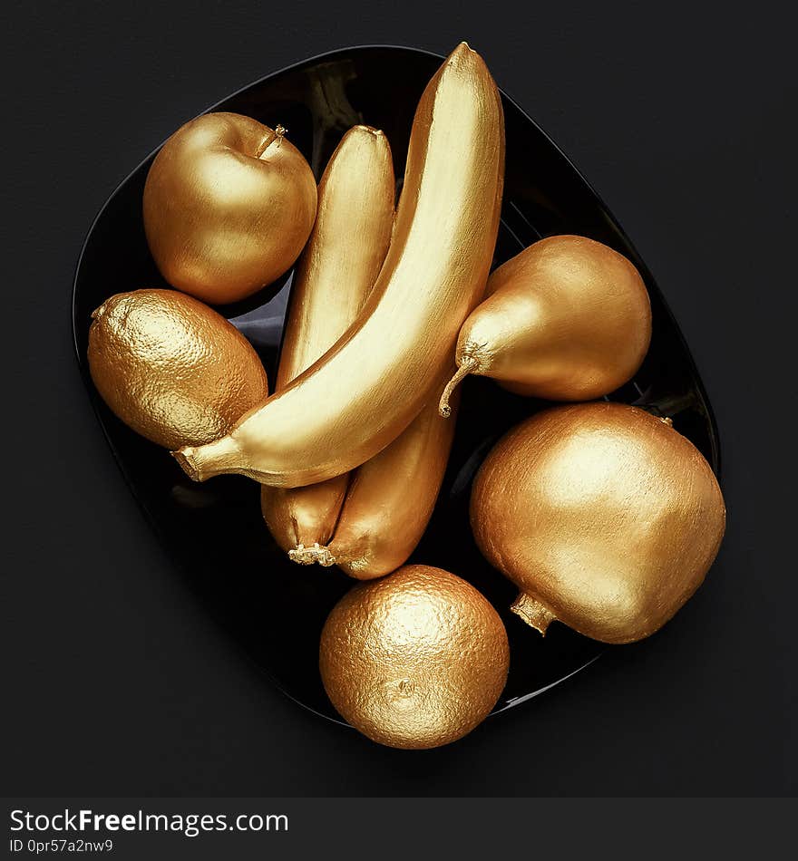 Fruits in golden glaze on plate over black background, top view.