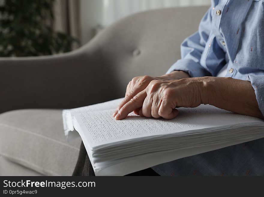 Blind senior person reading book written in Braille on sofa indoors, closeup. Space for text