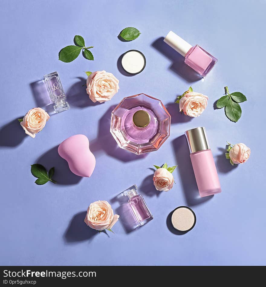 Flat lay composition with bottles of perfume, cosmetics and roses on color background