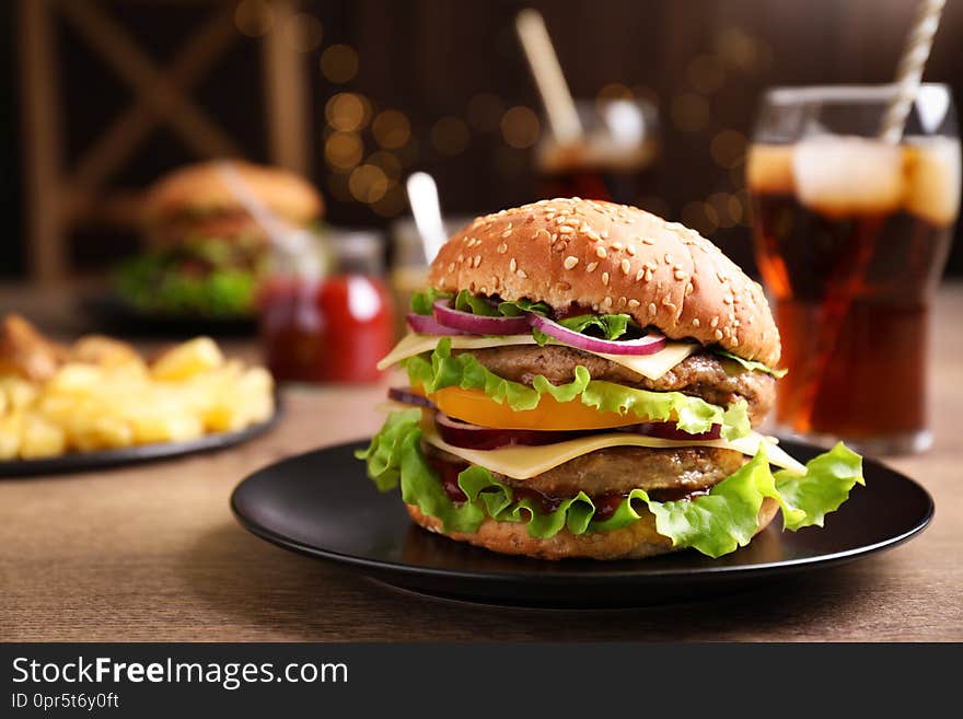 Plate with delicious hamburger on wooden table. Space for text