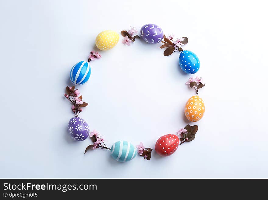 Frame made of painted Easter eggs and blossoming branches on white background, top view.