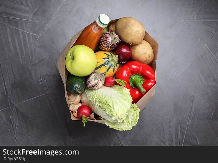 Paper package with fresh vegetables, apple and bottle of juice on dark background, top view