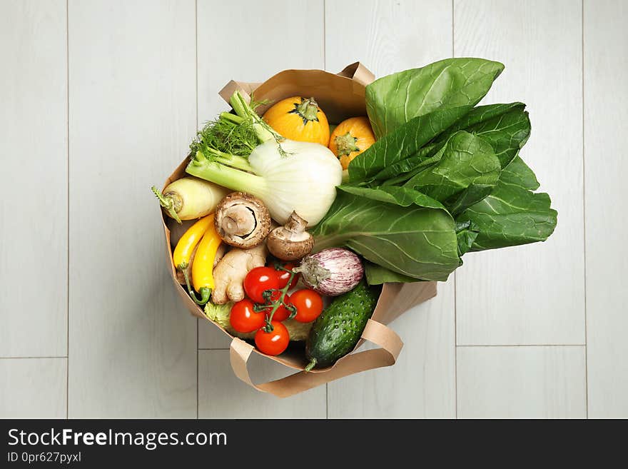 Paper bag full of fresh vegetables on light background, top view