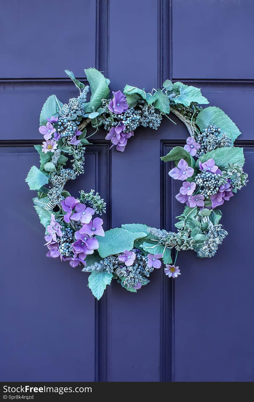 Close-up of beautiful green and purple wreath on deep purple wooden door.