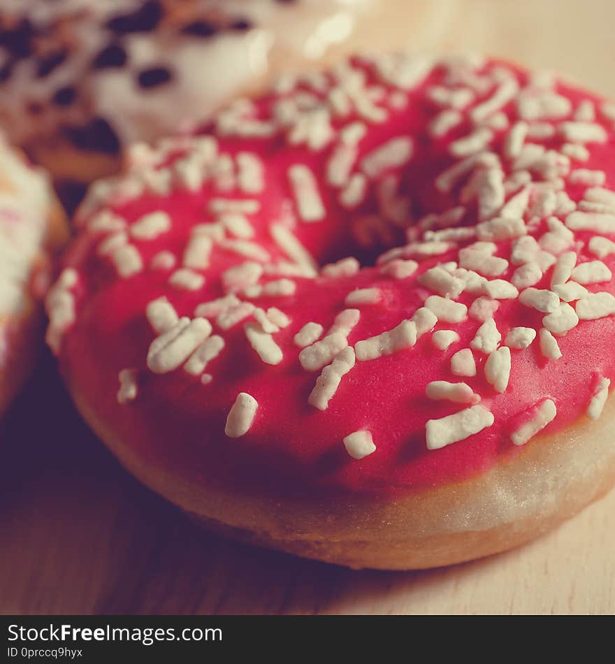 Pink glazed donut on wooden background and near rattan basket. Close up. Square format, toned