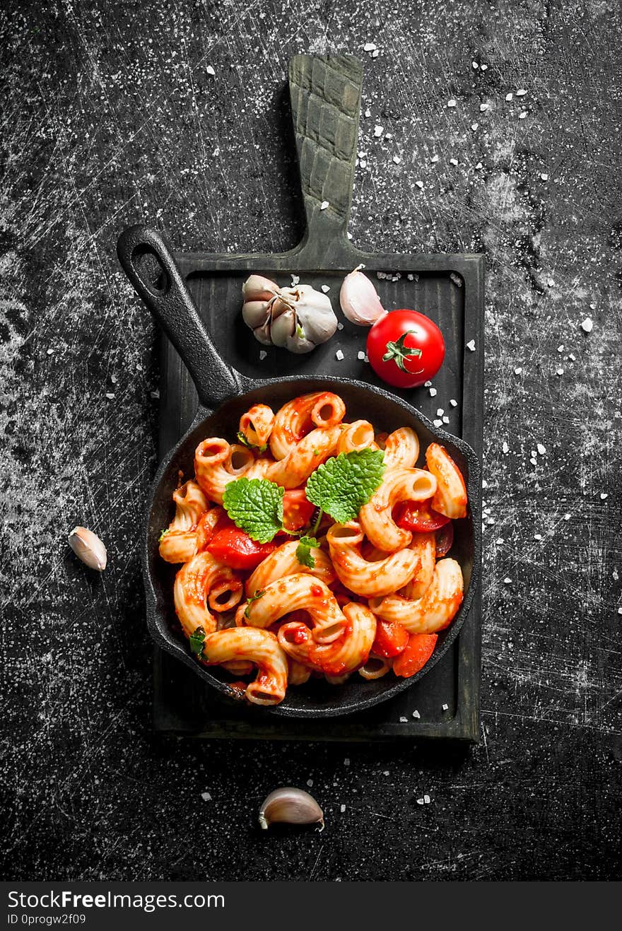 Pasta in pan on a cutting Board with garlic,tomato and mint leaves. On black rustic background