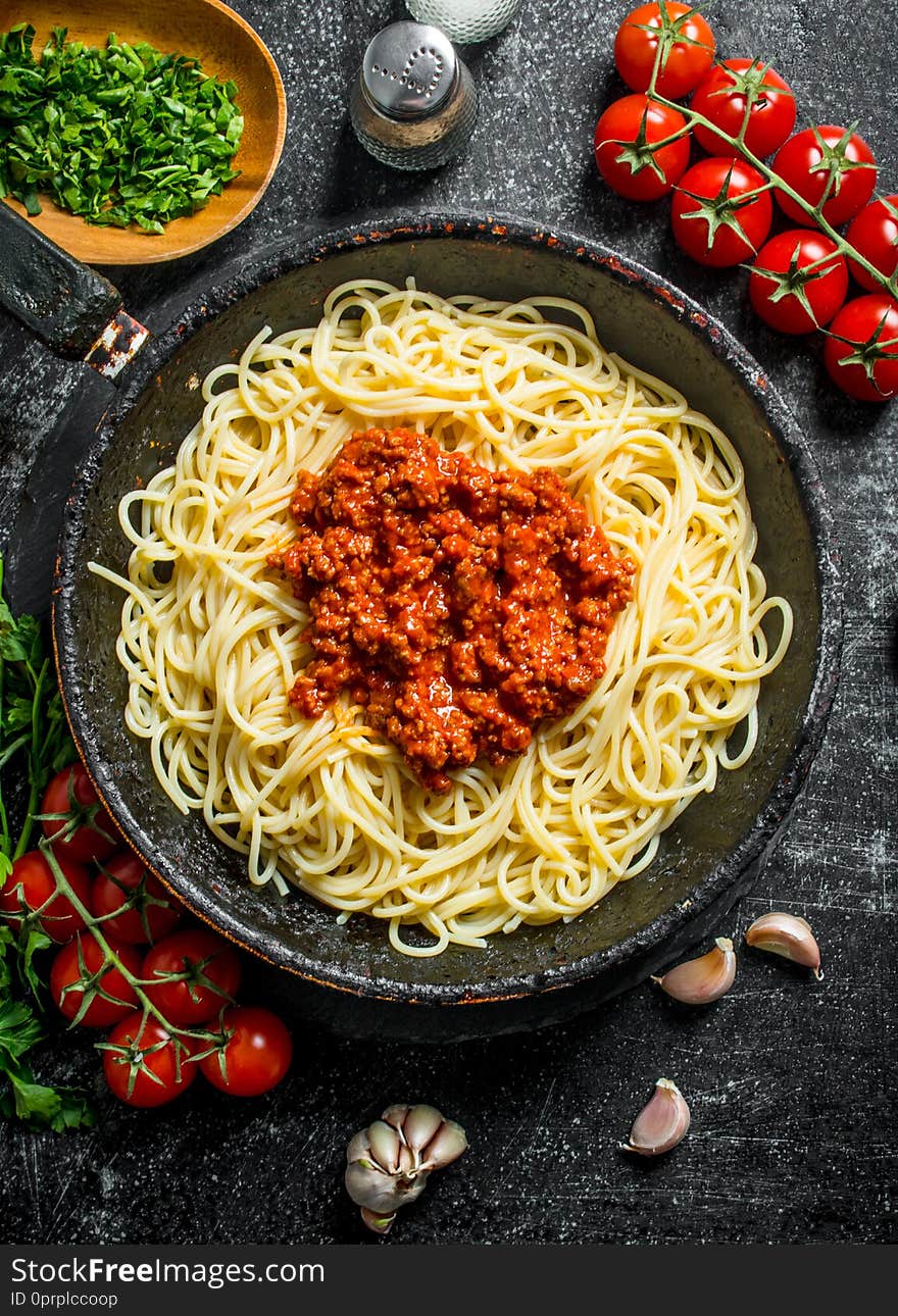 Spaghetti with Bolognese sauce with tomatoes and chopped greens in a bowl. On rustic background