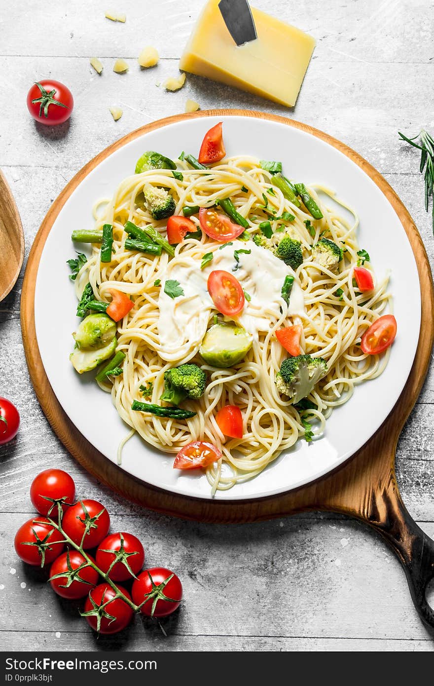 Pasta with vegetables and tomatoes on a branch. On white wooden background
