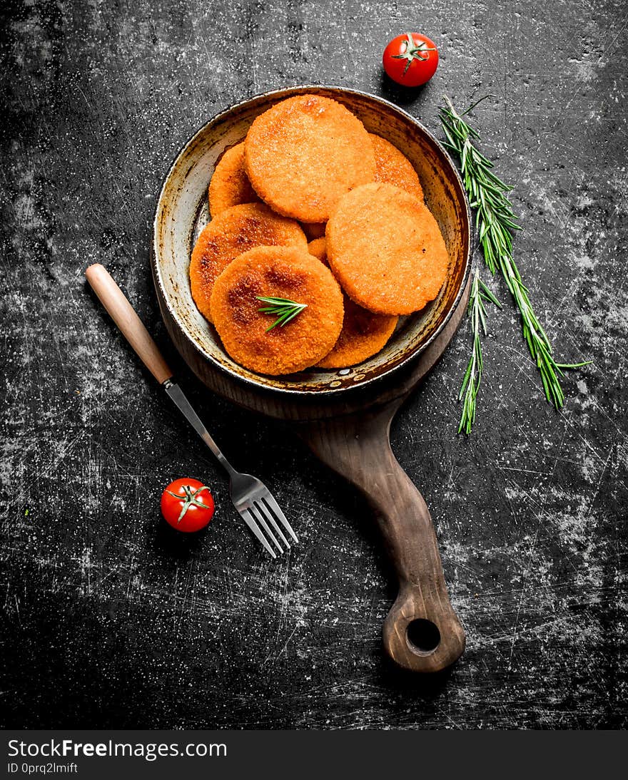 Fish cutlets in pan with fork and rosemary. On black rustic background