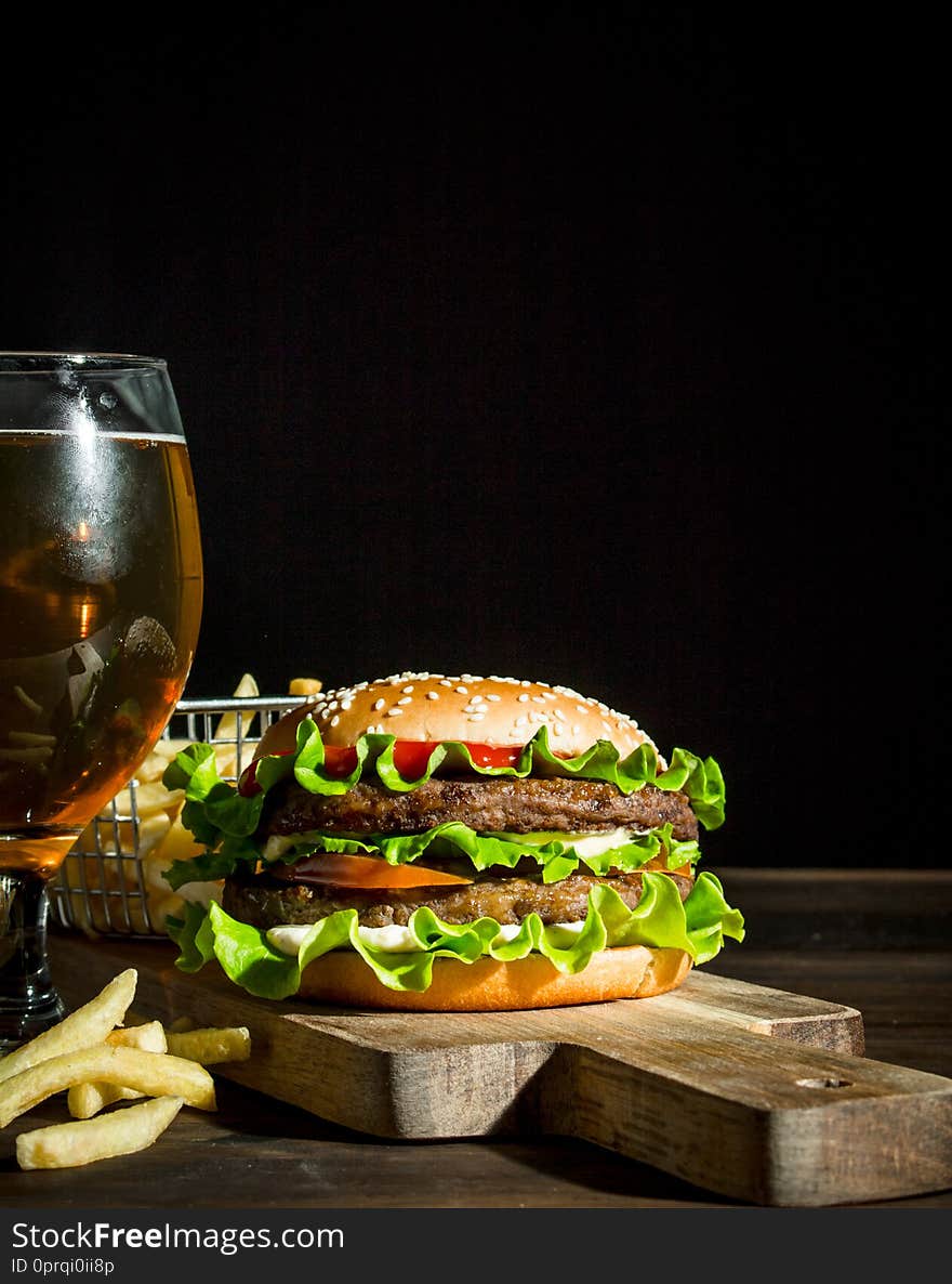 Burger with beer in a glass and fries. On wooden background
