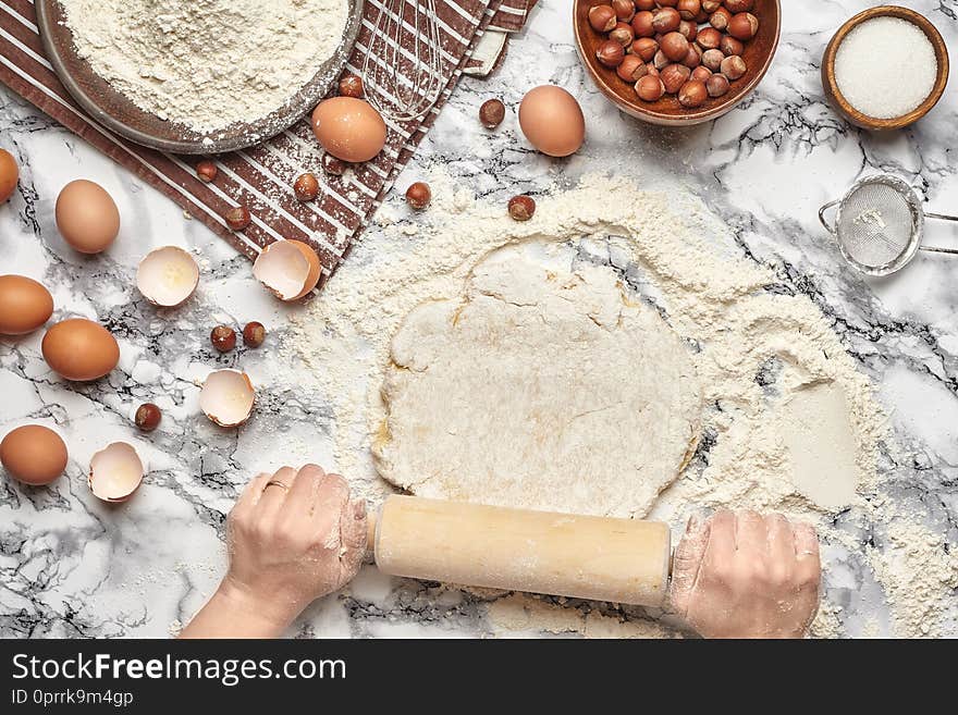 Close-up shot. Top view of a baker cook place, working with a raw dough, baking ingredients and kitchenware on the marble table background. Hands of a chef are roll out the dough with a rolling pin on the table. Close-up shot. Top view of a baker cook place, working with a raw dough, baking ingredients and kitchenware on the marble table background. Hands of a chef are roll out the dough with a rolling pin on the table.