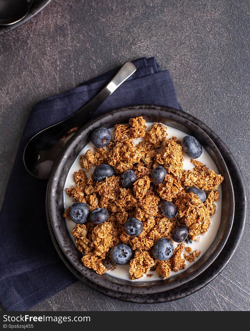 Overhead view of a bowl of granola with fresh blueberries and milk on a dark background. Overhead view of a bowl of granola with fresh blueberries and milk on a dark background