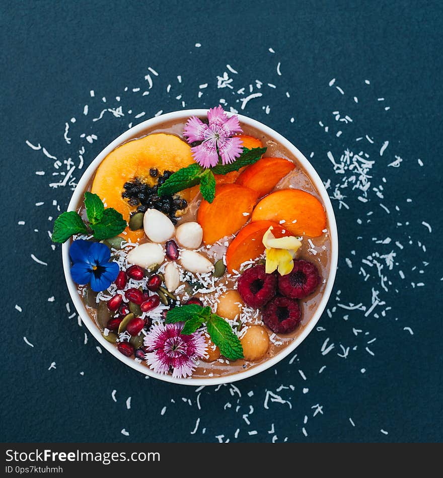 Isolated shot of bowl with tropical fruit decorated with flowers, mint, coconut flakes isolated over dark blue background. Fresh