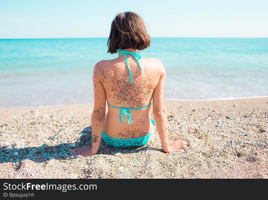 Girl on the beach with sand on his back looks at the ocean. fun on holidays in the sand