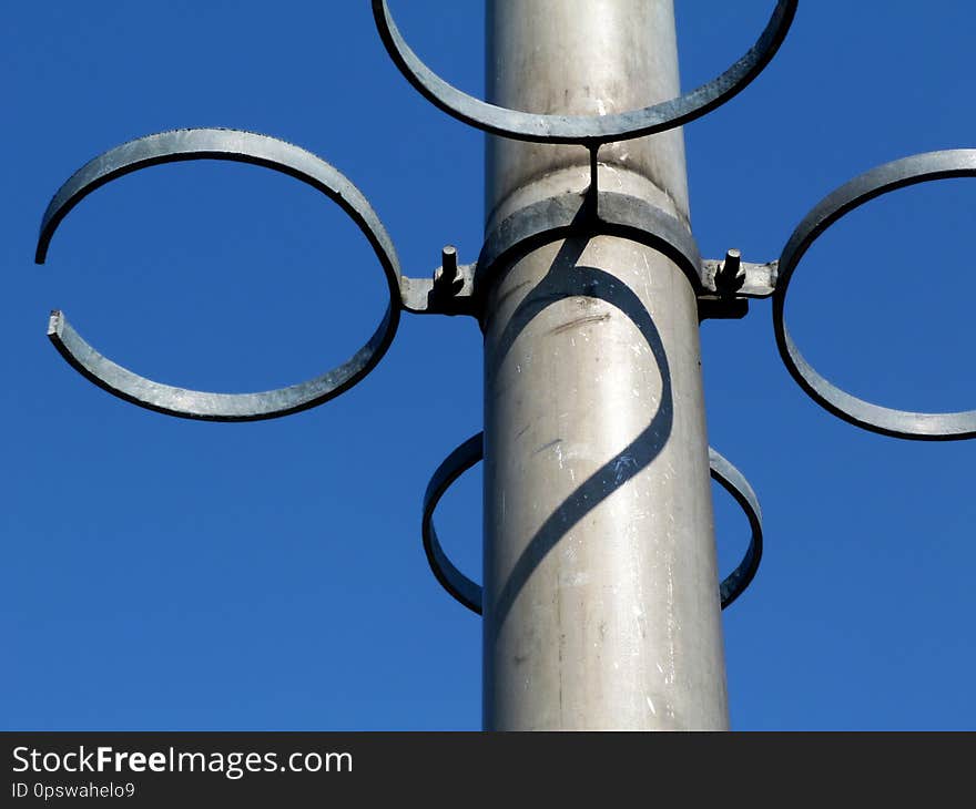 Empty steel rings of flower pot holders on aluminum light pole against blue sky background with strong shadow completing a heart shape. concept of you complete me. Empty steel rings of flower pot holders on aluminum light pole against blue sky background with strong shadow completing a heart shape. concept of you complete me