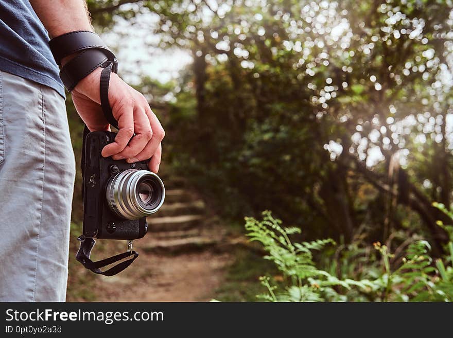Man is holding camera in his hand while walking by the path throw the green mountains.