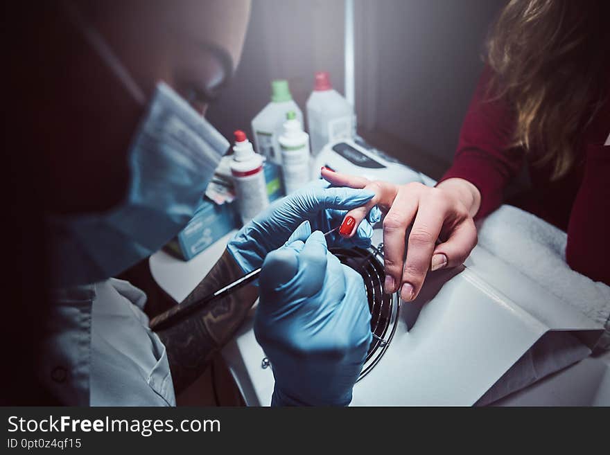 Beautician making long transparent artificial nails to a female client. Manicure procedure in a beauty salon