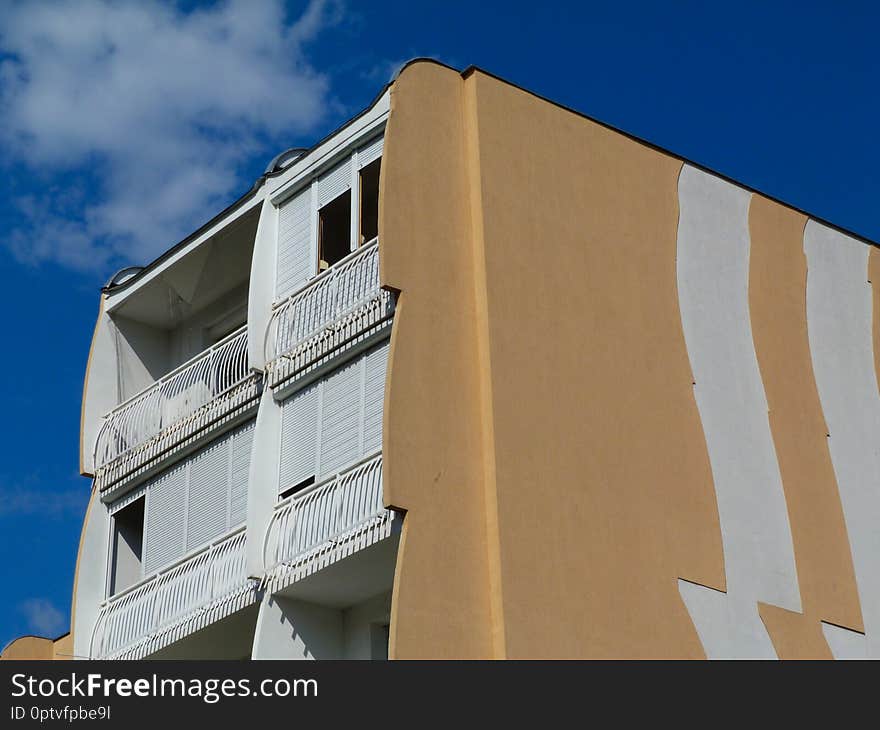 Part exterior elevation of concrete panel condominium building with blue sky above. trademark of multi unit residential architecture in Paks, Hungary. called the tulip building style. white balconies with roll down sun blind shades. Part exterior elevation of concrete panel condominium building with blue sky above. trademark of multi unit residential architecture in Paks, Hungary. called the tulip building style. white balconies with roll down sun blind shades.