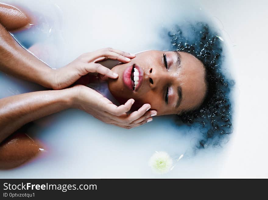 Young brown skin girl taking bath and lying in foam, wearing swimsuit.