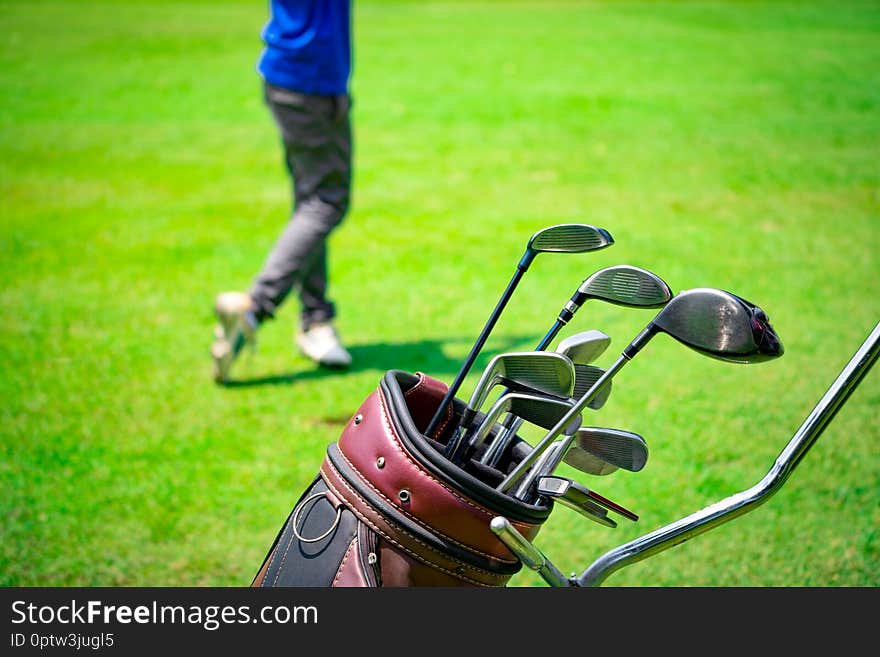 Golf club suit in bag cart and blurred golfer hitting golf ball on green golf course on summer time