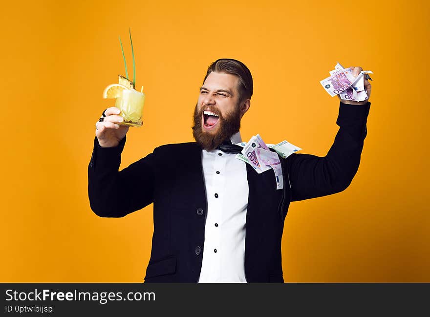 I am rich! Happy young businessman with glass of cocktail in formal clothes holding bunch of money banknotes and celebrating throwing money up